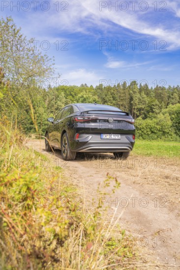 A black Volkswagen on a rural path with blue sky and forest, Cupra electric car, e-car sharing,