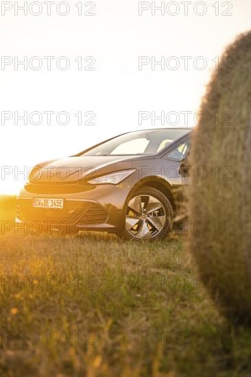 Car in the golden light of sunset in a meadow next to a hay bale, electric car Cupra, e-car