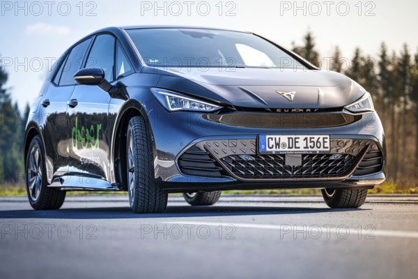 Black car on a road with forest in the background under clear sky, electric car Cupra, e-car