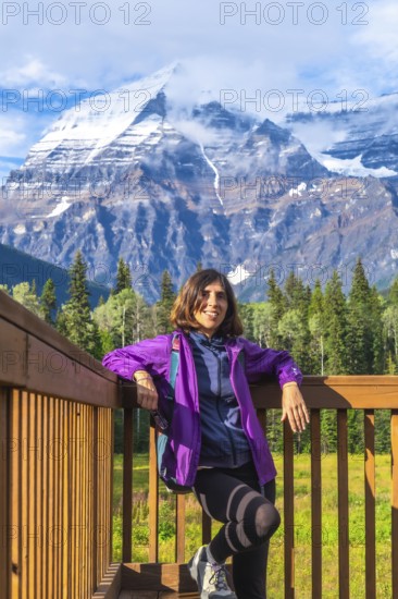 Female hiker is taking a break on a wooden platform, enjoying the breathtaking view of mount