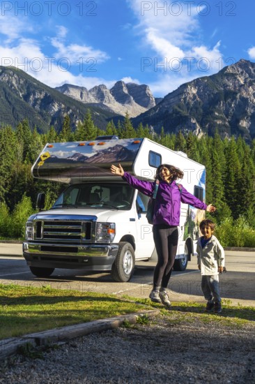 Happy mother and son are jumping in front of their recreational vehicle near mount robson in the