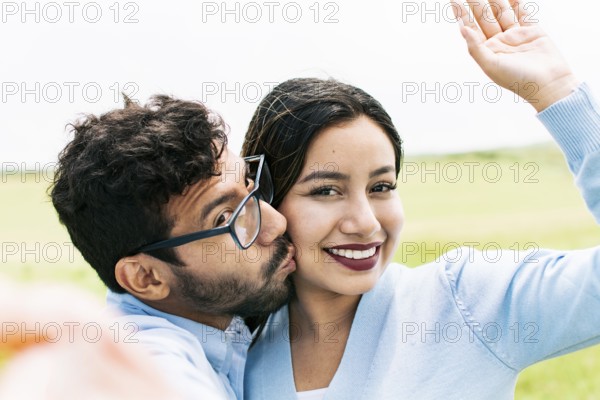 Selfie of young happy couple kissing in the field. Cute couple in love taking a selfie in the