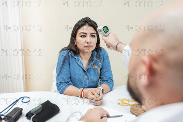 Doctor taking temperature to woman patient in office. Male doctor taking temperature with gun to