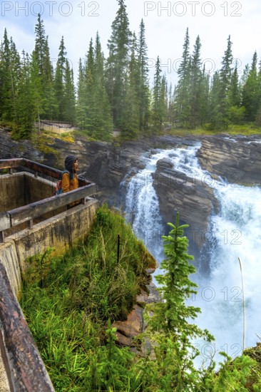 Hiker enjoying the breathtaking view of athabasca falls plunging into the canyon, surrounded by