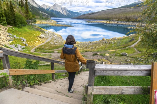 Female tourist walking down wooden stairs to medicine lake, with turquoise waters reflecting