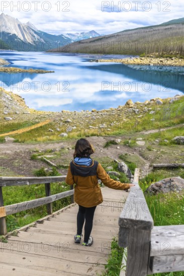 Female tourist walking down wooden stairs approaching medicine lake with turquoise water reflecting