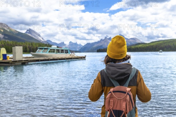 Female tourist wearing a yellow beanie and carrying a backpack admires the stunning view of maligne