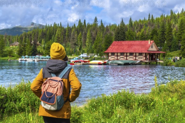 Female tourist wearing a yellow beanie and backpack admiring the iconic boathouse at maligne lake