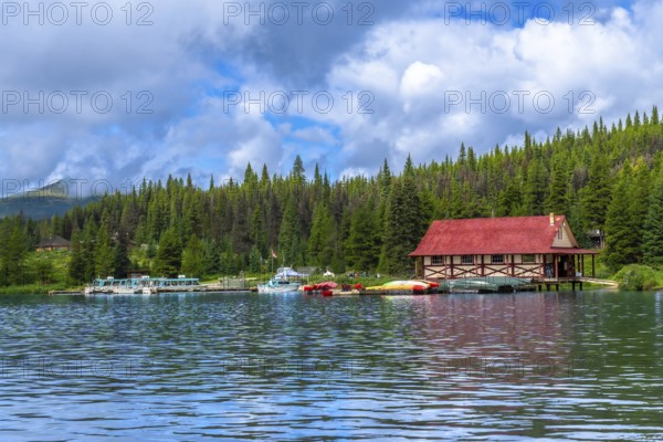 Colorful canoes and tour boats are docking at a boathouse with a red roof on maligne lake in jasper