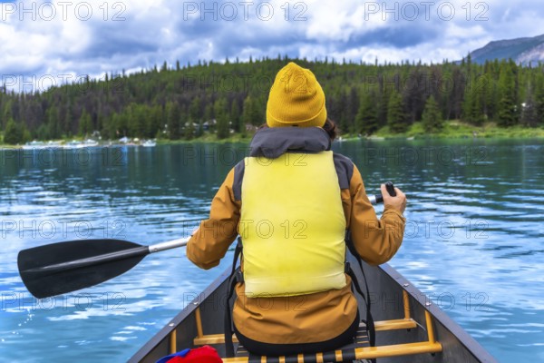 Tourist wearing yellow life jacket and beanie paddling a canoe in maligne lake, jasper national