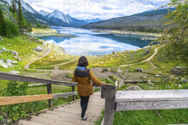 Female hiker descending wooden stairs towards the scenic medicine lake, surrounded by the canadian