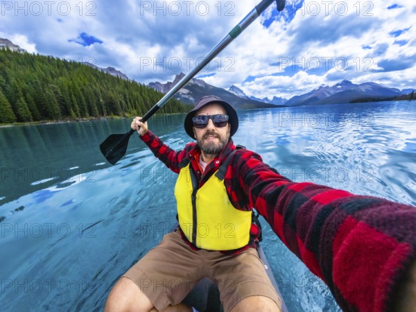 Tourist wearing sunglasses and life jacket kayaking and taking a selfie in maligne lake with