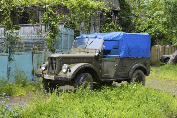 Old off-road vehicle with blue tarpaulin cover standing in overgrown green surroundings, Soviet