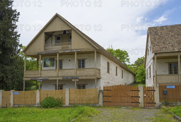 Traditional house with wooden balcony and fence in a rural setting with cloudy skies, village