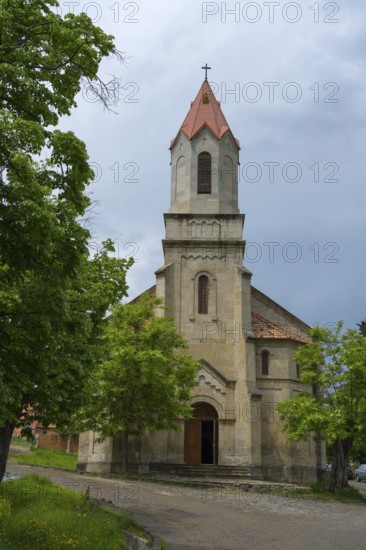 Large church with Gothic bell tower and red roof tiles surrounded by green trees, German