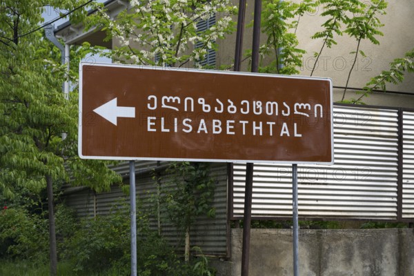 Brown road sign points towards Elisabeththal in Georgian and English letters, village founded by