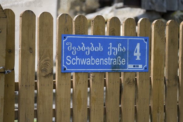 Blue street sign with house number 4 on a wooden fence in Georgian and German letters,