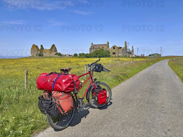 Bicycle with luggage on a dirt road in front of ruins amidst blooming countryside, South Uist,