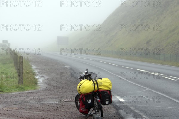 Bicycle with luggage on a foggy and deserted country road, cycle tourism, adventure, Shetlands,