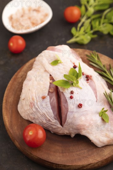 Raw Turkey Thigh with spices and rosemary on cutting board on black concrete background and linen