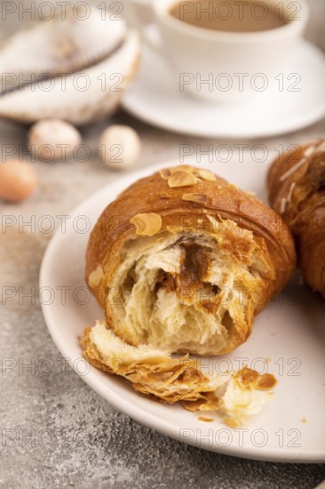 Croissant on white plate on brown concrete background and linen textile, cup of coffee, side view,