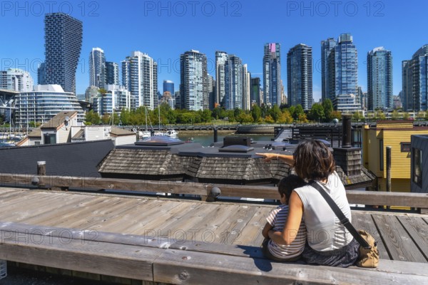 Mother and son sitting on a wooden boardwalk, pointing towards the stunning vancouver skyline from