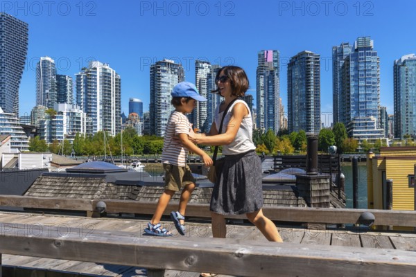 Mother and son enjoying a sunny day walking along the wooden boardwalk on granville island with the