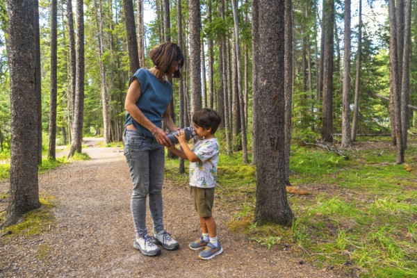 Mother giving a drink of water to her son from a reusable water bottle while hiking on a beautiful