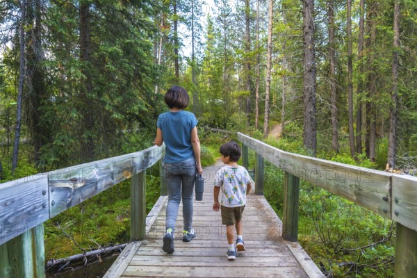 Mother and son enjoying a leisurely hike, crossing a picturesque wooden bridge amidst the lush