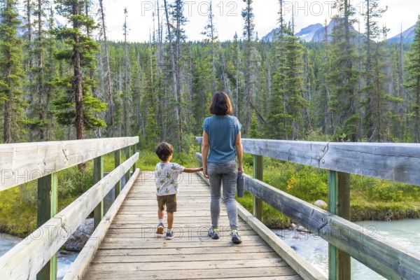 Mother and son holding hands, enjoying a leisurely hike across a wooden bridge, surrounded by the