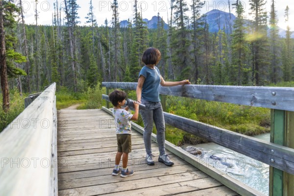 Mother and son using binoculars observing the landscape from a wooden footbridge over a creek in