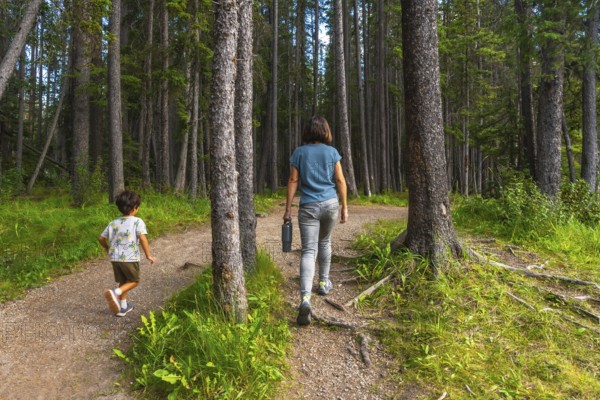 Mother carrying a water bottle and her son enjoying a leisurely hike along a picturesque forest