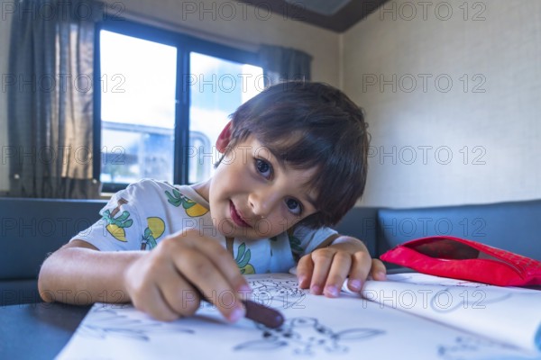 Young boy enjoys a creative moment, drawing with crayons in a camper van, surrounded by the natural