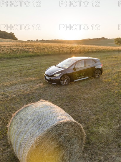 A black car is parked in a field next to a hay bale at sunset, deer e-car sharing, Cupra electric