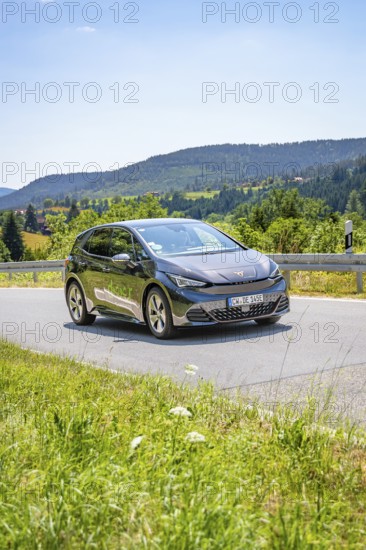 Black car driving on a road through a hilly landscape in daylight, deer e-car sharing, Cupra