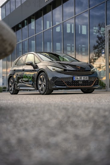 Black car in front of a modern building with glass façade, photographed on concrete floor, Deer