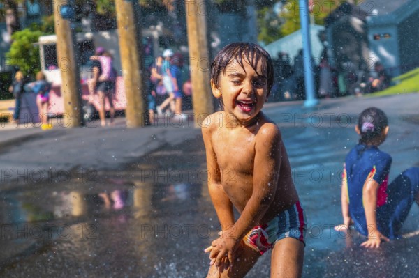 Cheerful child with wet hair and colorful swimming trunks laughing and playing in a city park