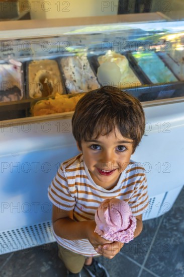Smiling child holding a strawberry ice cream cone in front of a display case full of colorful ice