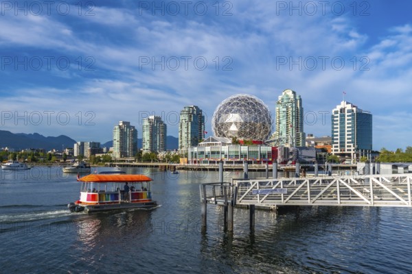 Passengers are enjoying a sunny day, riding an aquabus ferry in false creek with science world and