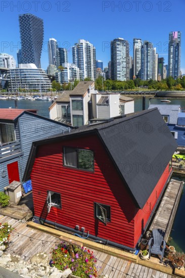 Red floating house with open windows and potted flowers on the deck with other floating homes and