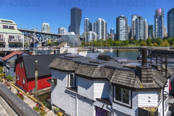 Colorful floating homes contrasting with vancouver's high rise skyline under a clear blue sky,