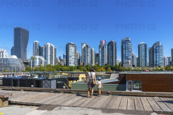 Mother and son standing on a wooden pier, admiring vancouver's modern skyline with high rise