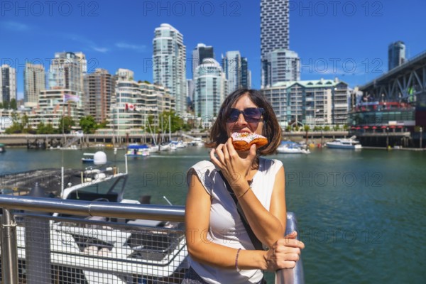 Young woman enjoying a delicious donut with the stunning cityscape of vancouver, british columbia,