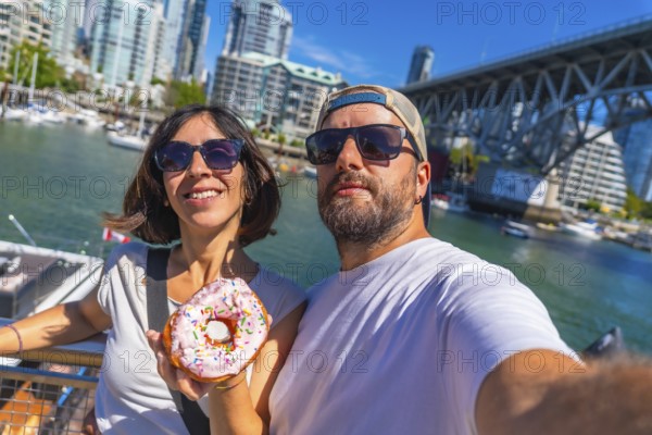 Happy tourists taking a selfie while holding a donut with sprinkles in front of the cityscape and