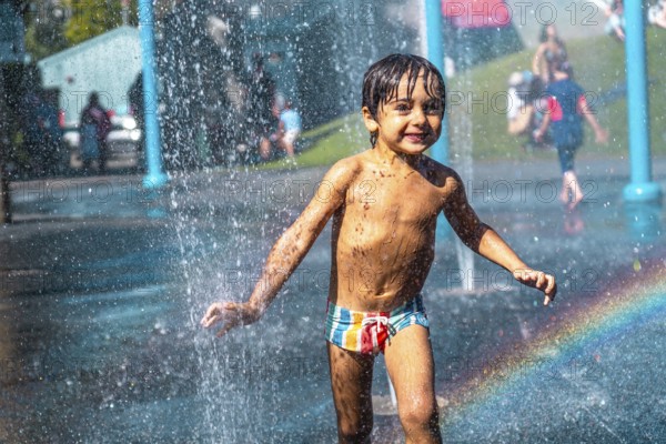 Happy muddy child playing and running through jets of water in a playground water park fountain in