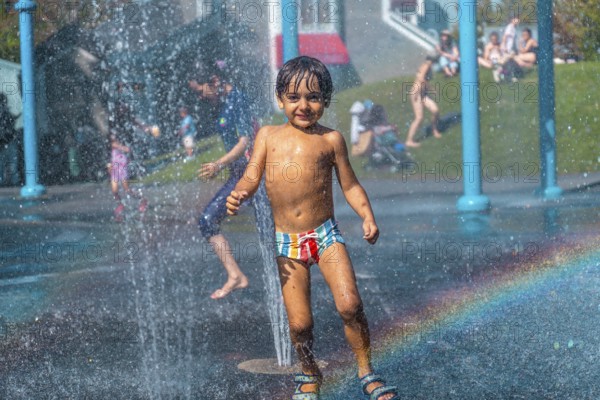Happy child playing and running under the water jets of a splash pad in vancouver, british