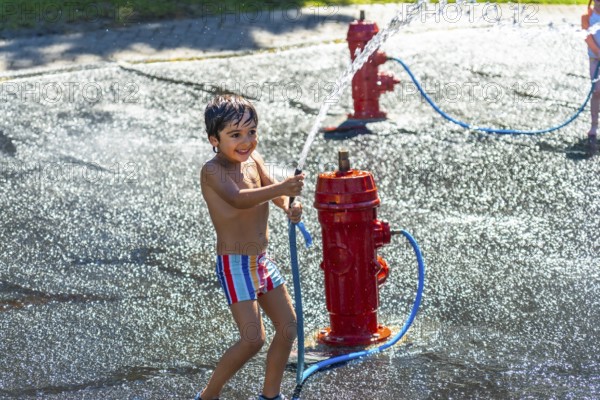 Happy child playing and splashing with water jets coming out of a small red fire hydrant during a
