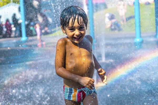 Happy child running and playing under splash pad jets with rainbow in the background on a hot