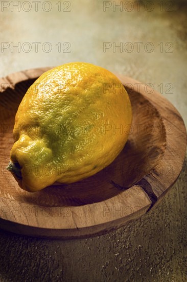 A vibrant lemon with a textured skin sits on a handcrafted wooden plate, illuminated by gentle