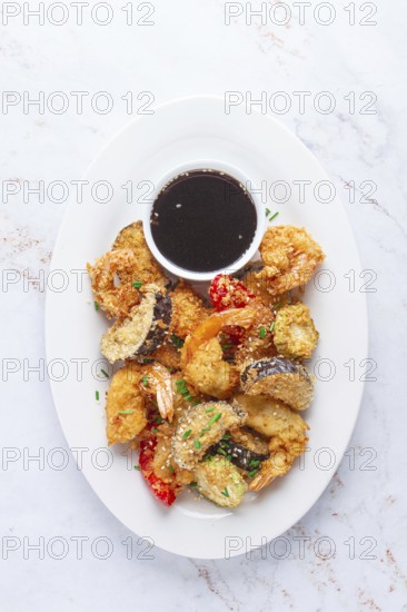 Shrimp and assorted vegetables are deep fried in a light batter and served on a white plate. A